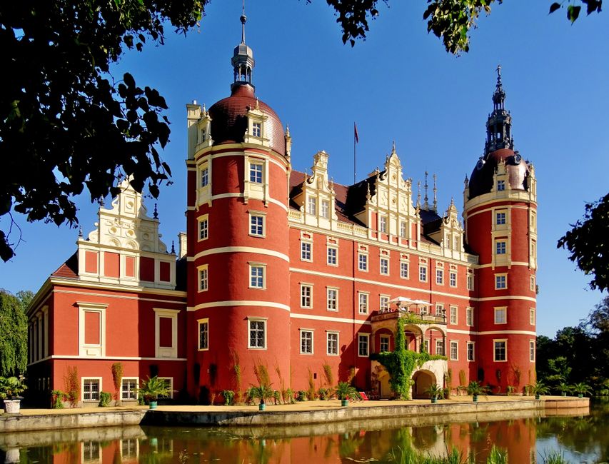 Stunning view of Muskau Castle reflecting in the canal under a clear blue sky.