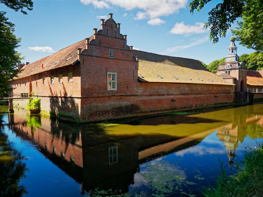 A historical brick castle with a moat and clear reflection under a bright sky.